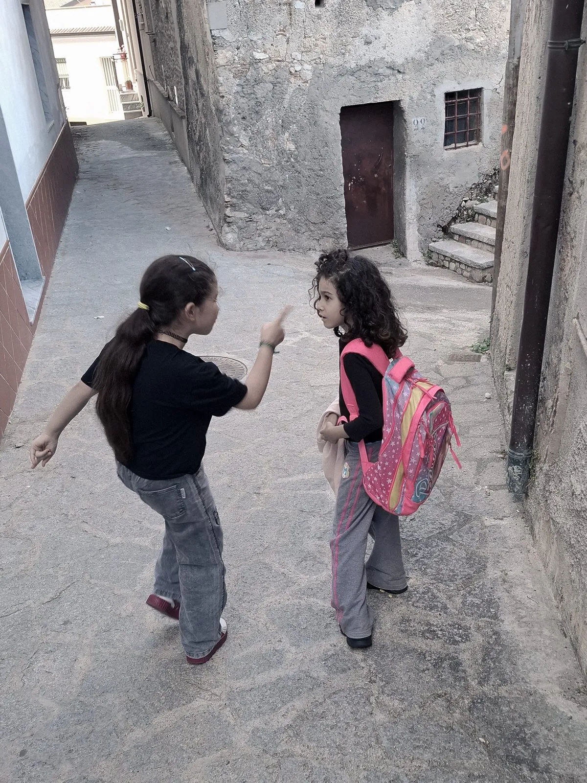 Deux fillettes discutent dans une ruelle de Camini, cartable sur le dos
